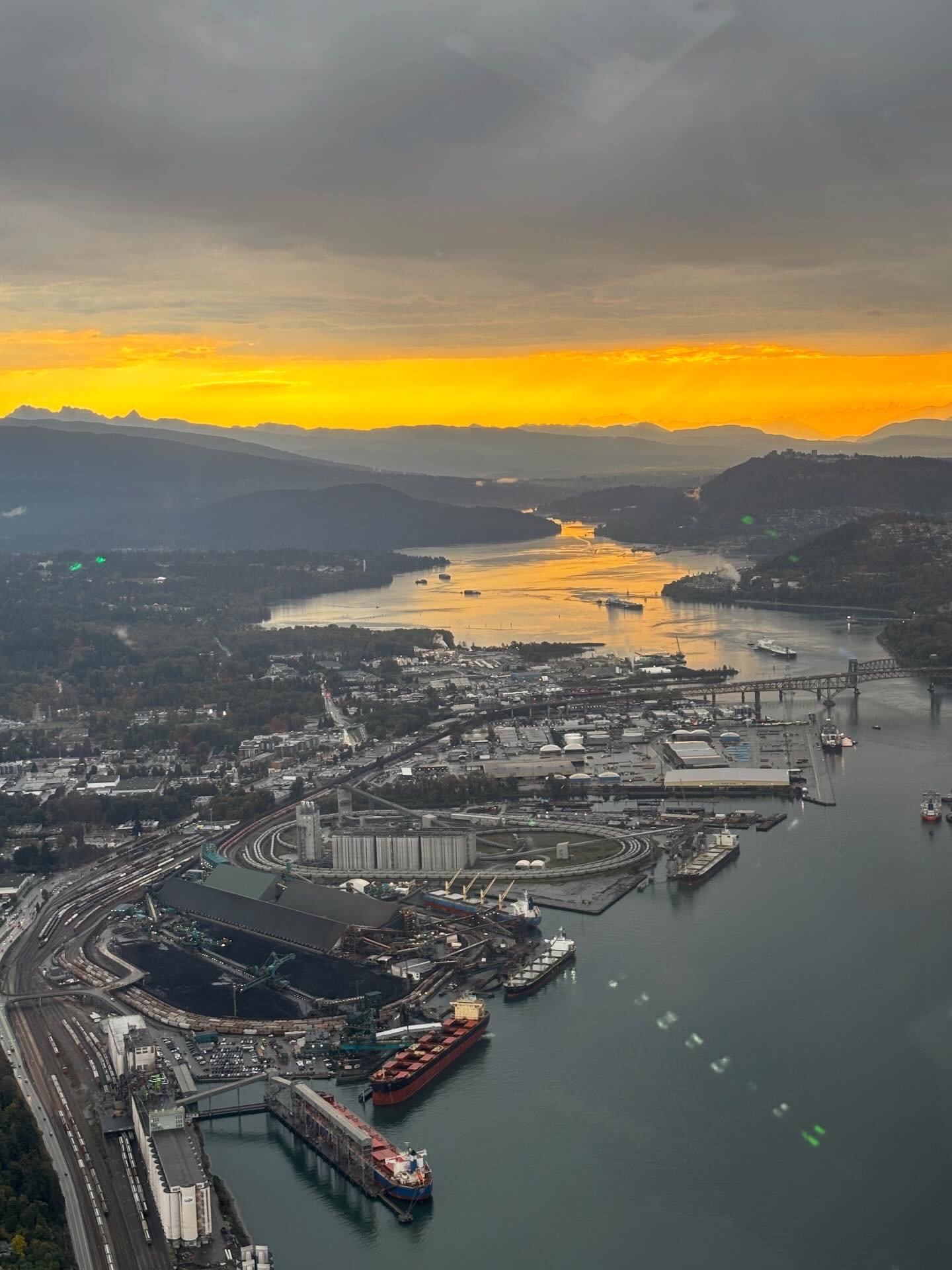 Aerial sunset over Burrard Inlet and Vancouver port with mountains in background