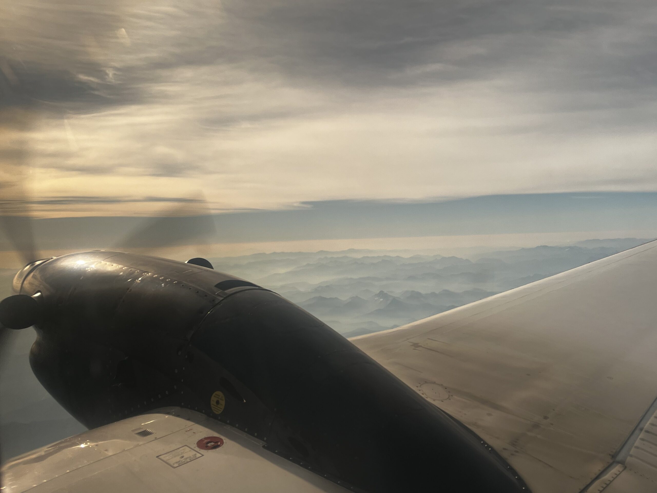 Turboprop engine and wing visible through airplane window over British Columbia mountains